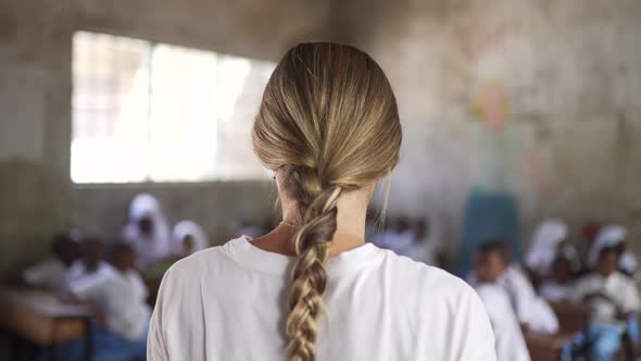 Not recognizable white caucasian blonde girl teaching as a volunteer in african school with little c