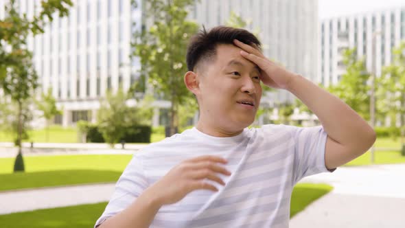 A Young Asian Man Celebrates in an Urban Area  a Park and Office Buildings in the Blurry Background