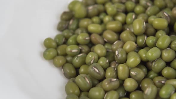 Green Mung beans fall and fill a white ceramic plate. 