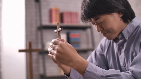 A young Asian Christian man praying to Jesus Christ in a church.