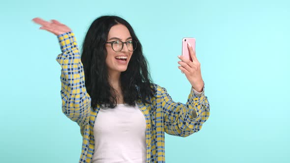Cheerful Young Woman in Glasses Talking on Video Call Waving Hand at Smartphone Front Camera and