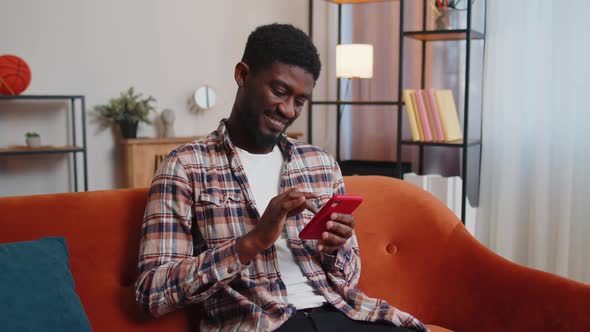 Joyful Young Adult Man Sitting on Sofa Using Smartphone Watching Video Online Shopping Tapping
