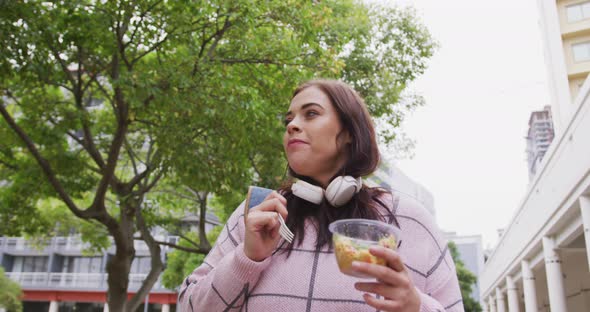 Young Caucasian woman eating and walking