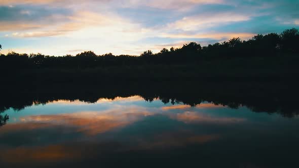 Aerial drone video of a glassy lake with cotton candy sky.