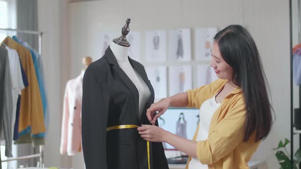 Smiling Asian Female Designer Measuring Business Jacket On A Mannequin While Designing Clothes