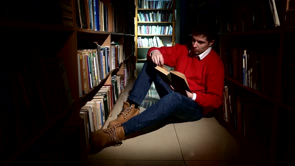 Student Sitting on Floor in Library, Reading Book. Close Up