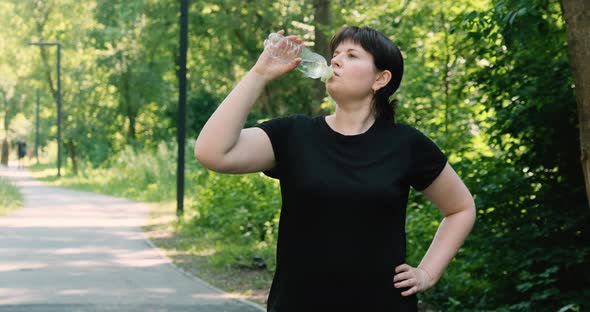 Young Plussize Woman Plays Sports in the Park and Drinks Water