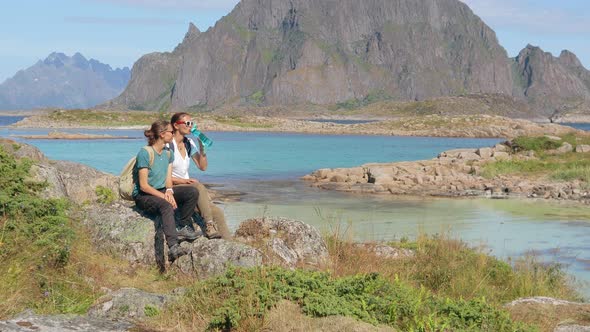 Two Young Women Travelers Sitting on the Rock and Drinking Water From the Bottle