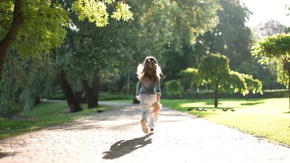 Tracking Shot of Happy Carefree Little Girl Running Jumping in Slow Motion in Sunbeam in Park