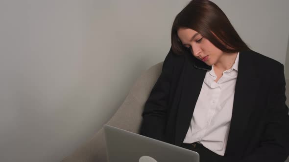 Focused Businesswoman Talking on a Mobile Phone While Working on a Laptop