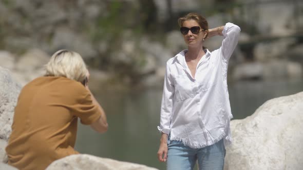 A Male Photographer Takes a Photo of a Woman in Nature By a Stream