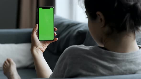 Woman at Home Lying on a Couch using Smartphone with Green Mock-up Screen. Girl Using