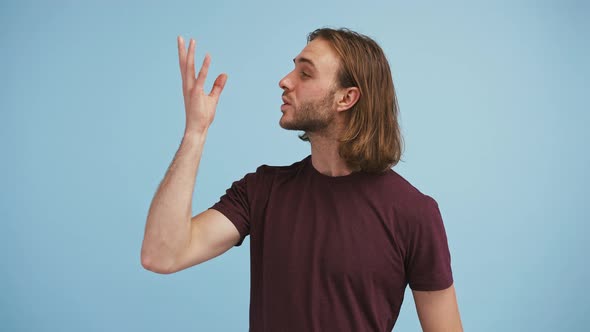 Young Guy in Brown Tshirt is Showing Bellissimo Hand Gesture and Smiling While Posing Against Blue