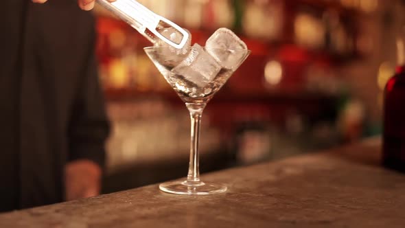 Bartender putting ice cubes into martini glass