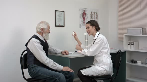 Smiling Pharmacist Holding a Bottle of Pills and Pointing Them To Senior Patient