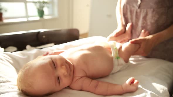 Mother Doing Exercises for Her Newborn Baby in a Diaper- Working with His Legs