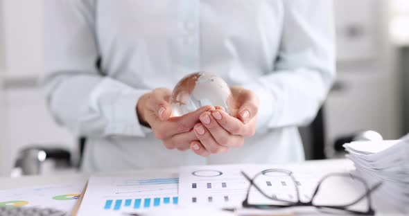 Businesswoman Holds Glass Globe in Hands on Business Graphics Table Closeup