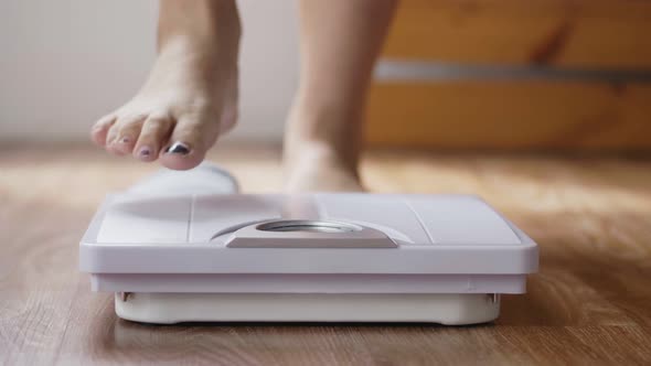 Close up of young Asian woman checking body weight on weighing scale in the living room at home.