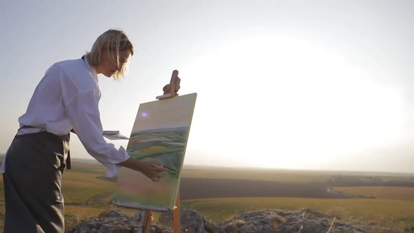 Beautiful field at sunset. Young girl artist who paints a picture of nature.