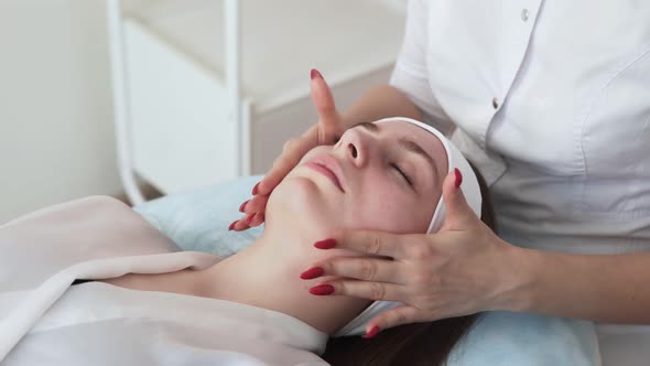 Hands of Beautician Applying Cream on Face of Woman Lying with Closed Eyes on Couch