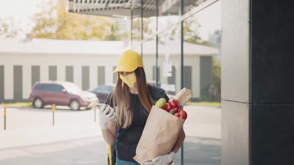 Young Delivery Worker Woman in Uniform Hat Medical Mask Gloves Holding Bag with