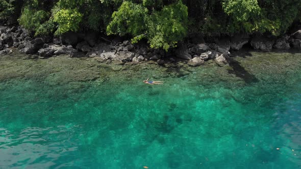 Aerial: woman snorkeling on Pulau Gunung Api coastline coral reef tropical