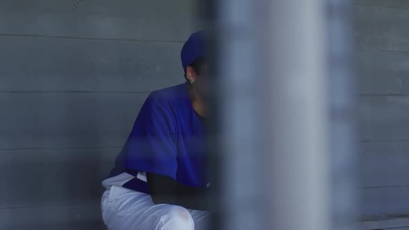 Nervous mixed race female baseball player, sitting on bench waiting, holding baseball bal