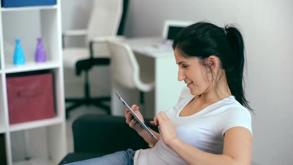 Beautiful Woman Using Tablet Sitting on Sofa at Home