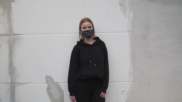 Young Female in Black Clothes and Face Mask Standing by Wall Looking at Camera. Slow Motion