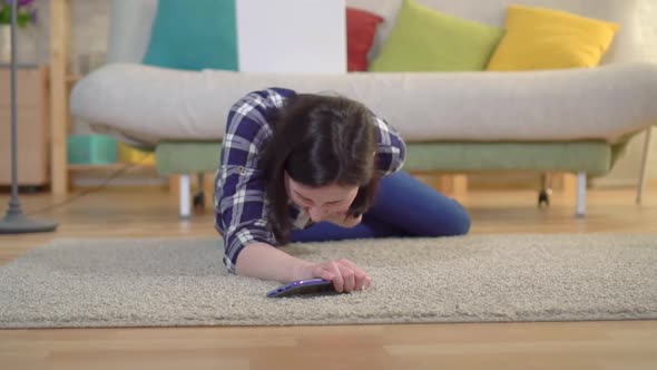 A Young Woman in a Shirt Had a Heart Attack and She Tries To Reach the Smartphone Lying on the Floor