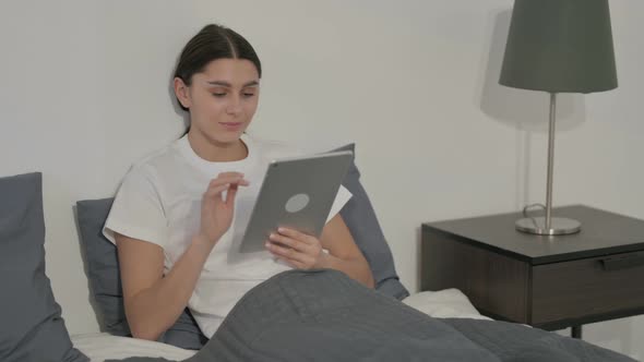 Hispanic Woman using Tablet while Sitting in Bed