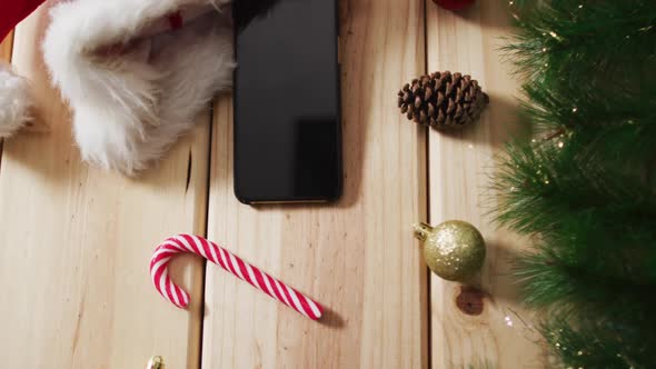 Video of christmas decorations with smartphone and santa hat on wooden background