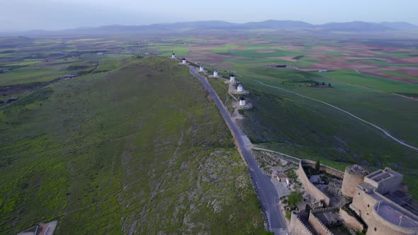 Old white windmills in line on top of a green hill in a traditional Spanish village. Aerial view