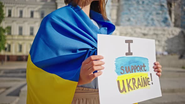 Woman Holds Poster Standing on Square at Historical Monument