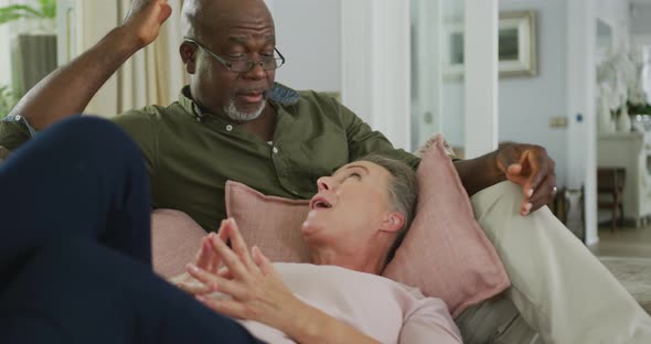 Happy senior diverse couple wearing shirts and watching tv in living room