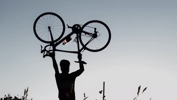 Silhouette of Man Cyclist Lifts the Bicycle As a Symbol of Victory