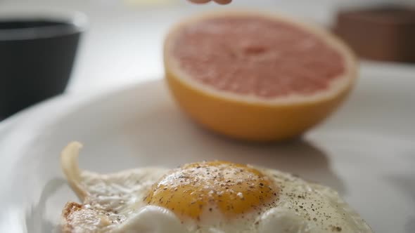 Sprinkling Fine Salt on Medium-Cooked Sunny Side Up Egg with Grapefruit on Side