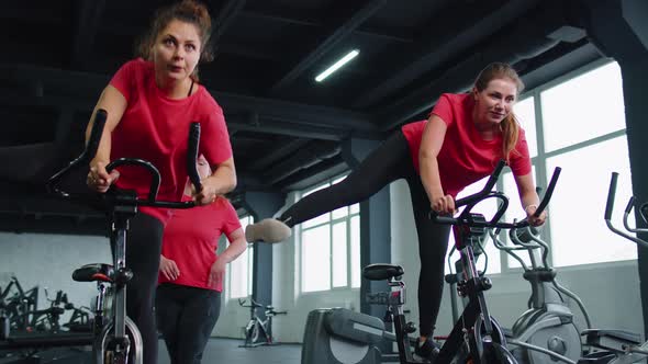 Group Athletic Girls Performing Aerobic Riding Training Exercises on Cycling Stationary Bike in Gym