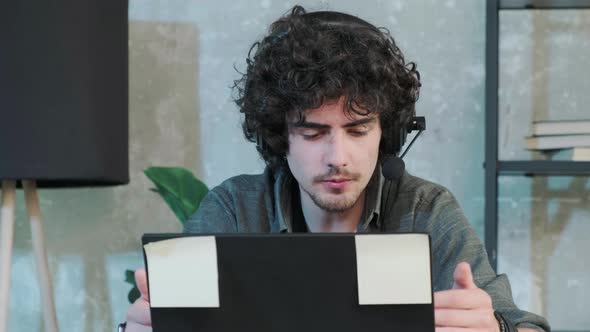 Young Curly Haired Man Using Laptop Computer with Headset to Talking Online