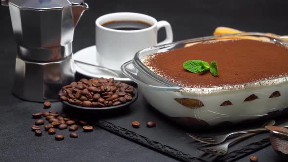 Tiramisu Dessert in Baking Dish, Coffee Maker, Savoiardi Cookies and Cup of Espresso on Concrete