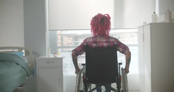 Young Woman with Pink Hair Riding in Wheelchair in Hospital