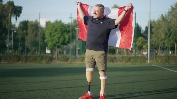 Joyful Happy Male Amputee with Canadian Flag Standing on Sunny Sports Field Looking Away Smiling