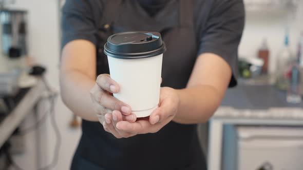 Hands of barista giving takeaway coffee cup to customer in the cafe.