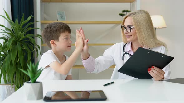 Smiling Senior Female Family Doctor in Uniform Consulting Little Kid Patient at Checkup Meeting in