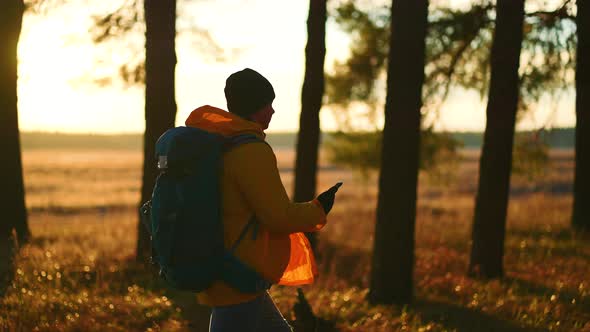 Man Hiker Backpacker Traveler Camper with Her Phone Looks at a Map or Route Under Sun Light