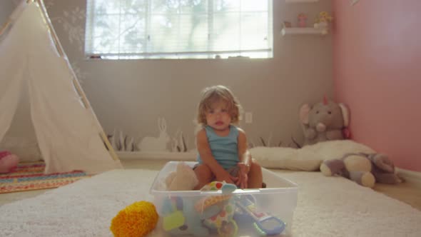 Little Girl Sitting with Toys Covers Camera Lens with Her Hand