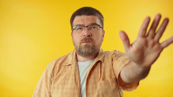 Caucasian bearded man in yellow shirt confidently saying no on camera over colorful background