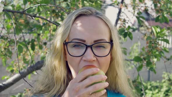 portrait of a young woman biting and eating a ripe green apple, looking at the camera in the garden,