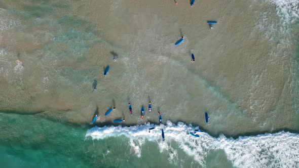 Aerial drone shot looking down on a large group of people learning to surf at the beach