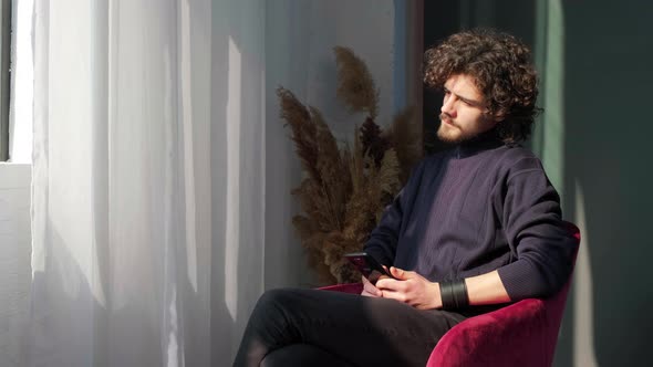 Man Sitting Near Window and Writing a Sms on Background of Sunset